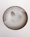 A round ceramic plate with a matte, speckled finish, featuring a dark brown rim and subtle hand-painted gray and brown accents on the interior, shown against a plain white background. Scree Ceramics | Fodder | Hope Collection