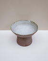 A handmade ceramic pedestal bowl with a textured, earthy brown base and a light gray glazed interior, set against a neutral beige and white background. Scree Ceramics | Fodder | Hope Collection