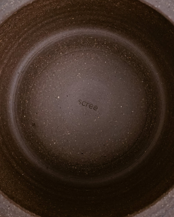Close-up top-down view of the inside of a dark brown speckled ceramic pot or pan, showing the brand name 'scree' printed in the center. Scree Ceramics | Fodder | Hope Collection