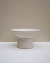 A speckled ceramic pedestal bowl in a warm off-white glaze, set against a minimalist beige and white studio background. Scree Ceramics | Fodder | Hope Collection