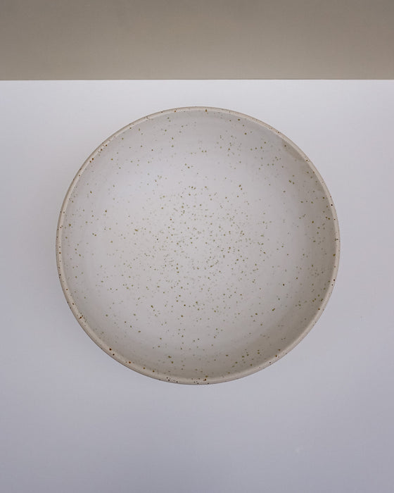 A round ceramic bowl with a speckled beige and brown glaze, photographed from directly above on a white surface with a beige background strip at the top. Scree Ceramics | Fodder | Hope Collection