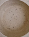Close-up of the inside of a speckled ceramic pot or container, showing a light beige interior with dark brown and black flecks and a faint embossed brand name in the center. Scree Ceramics | Fodder | Hope Collection