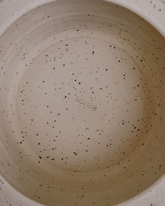 Close-up of the inside of a speckled ceramic pot or container, showing a light beige interior with dark brown and black flecks and a faint embossed brand name in the center. Scree Ceramics | Fodder | Hope Collection