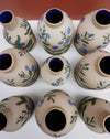 A group of small ceramic bottles or vases with a speckled beige body, decorated with blue flowers and green leaves, and finished with a dark blue glazed interior. Sophie Alda | Hope Collection | Shop Fodder