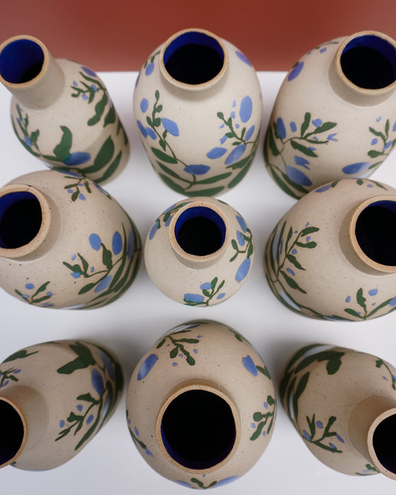 A group of small ceramic bottles or vases with a speckled beige body, decorated with blue flowers and green leaves, and finished with a dark blue glazed interior. Sophie Alda | Hope Collection | Shop Fodder