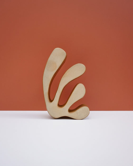 A minimalist abstract ceramic sculpture with a light natural wood finish, displayed on a white surface against a terracotta-colored background. Studio ERS Ceramics | Hope Collection | Shop Fodder