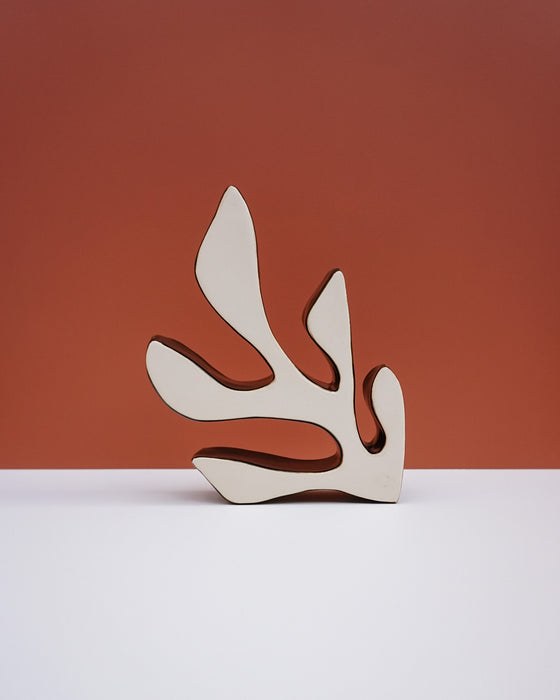 A minimalist abstract wooden sculpture with organic, leaf-like cutouts, standing on a white surface against a terracotta-colored background. Studio ERS Ceramics | Hope Collection | Shop Fodder