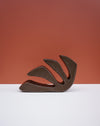 A sculptural, abstract leaf-shaped decorative object with a textured dark brown finish, displayed on a clean white surface against a terracotta-colored background. Studio ERS Ceramics | Hope Collection | Shop Fodder
