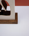 Close-up of a decorative object with a cream-colored upper section, dark brown abstract cutout details, and a medium brown wooden base on a white surface with a terracotta-colored background block. Studio ERS Ceramics | Hope Collection | Shop Fodder