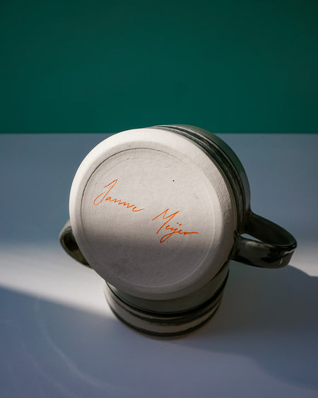 Ceramic mug with a signature on the lid against a gradient background.  Janne Meijer Ceramics | Shop Fodder