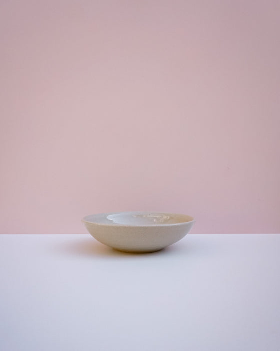 A small ceramic bowl with a textured, speckled off-white glaze, sitting on a white surface against a soft pink background. Lily Pearmain | Fodder