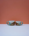 Two ceramic mugs with geometric pattern on a white surface and orange background. Liz Vidal Ceramics | Shop Fodder