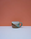 Ceramic mug with geometric design on a white surface and orange background. Liz Vidal Ceramics | Shop Fodder