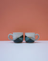 Two ceramic mugs with geometric design on a white surface and peach background. Liz Vidal Ceramics | Shop Fodder