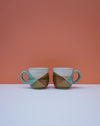Two ceramic mugs with a geometric design on a white surface and orange background. Liz Vidal Ceramics | Shop Fodder