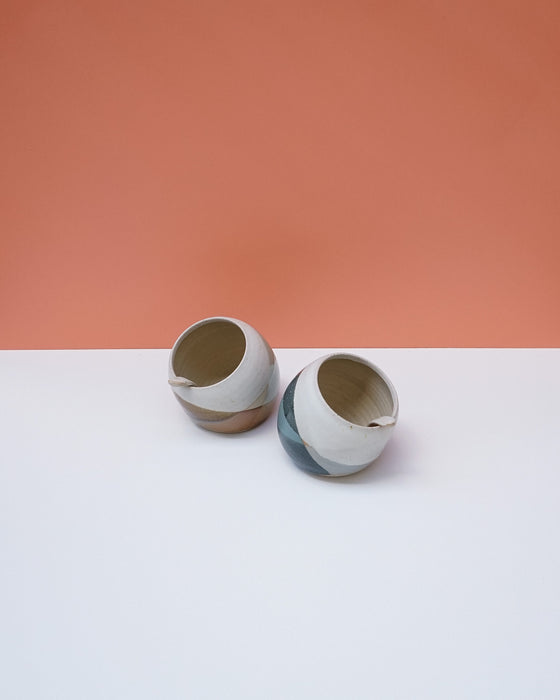 Two ceramic pots on a white surface with a peach-colored background. Liz Vidal Ceramics | Shop Fodder