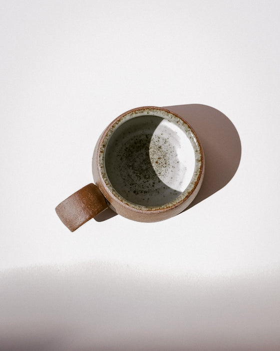 A single ceramic mug with a brown speckled exterior and a speckled gray-green glazed interior, photographed from above on a white background with a soft shadow. Short Loop Mug | Scree Ceramics | Fodder