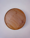 A round wooden tray with a textured pebbled leather-like finish, photographed from directly above on a plain light background. London Plane wooden cake stand by Selwyn House - lacewood grain - Fodder