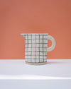 Ceramic pitcher with grid pattern on a peach and white background. Sophie Alda | Handmade Ceramics | Shop Fodder