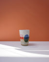 Ceramic cup with colorful design on a white surface and orange background. Sophie Alda | Handmade Ceramics | Shop Fodder
