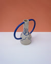 Ceramic vase with blue handles on a white surface against an orange background. Sophie Alda | Handmade Ceramics | Shop Fodder