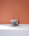 Ceramic coffee dripper with blue leaf designs on a white surface against an orange wall. Sophie Alda | Handmade Ceramics | Shop Fodder