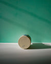 Round wooden object with a brand logo on a green background. Sophie Alda | Handmade Ceramics | Shop Fodder