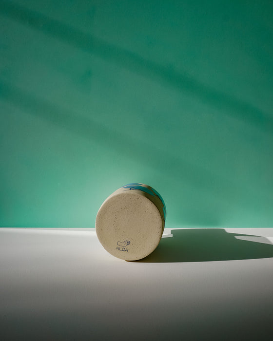 Round wooden object with a brand logo on a green background. Sophie Alda | Handmade Ceramics | Shop Fodder