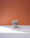 Ceramic cup with blue floral design on a white surface with an orange background. Sophie Alda | Handmade Ceramics | Shop Fodder