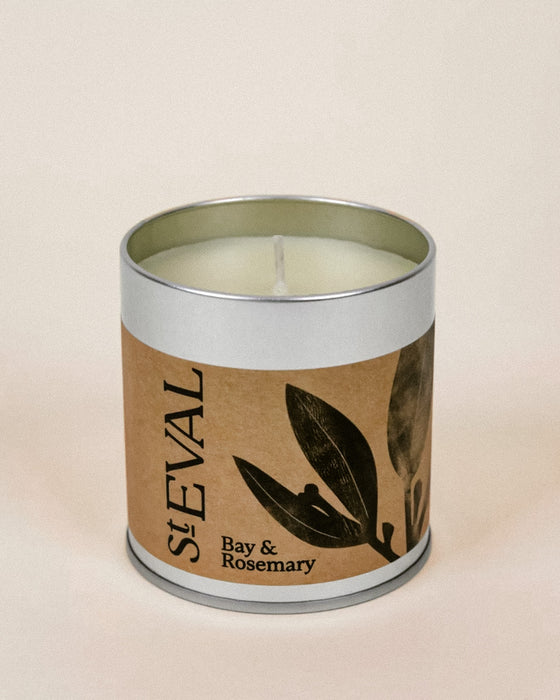 A St Eval Bay & Rosemary scented candle in a silver metal tin with a brown kraft paper label featuring black leaf illustrations.