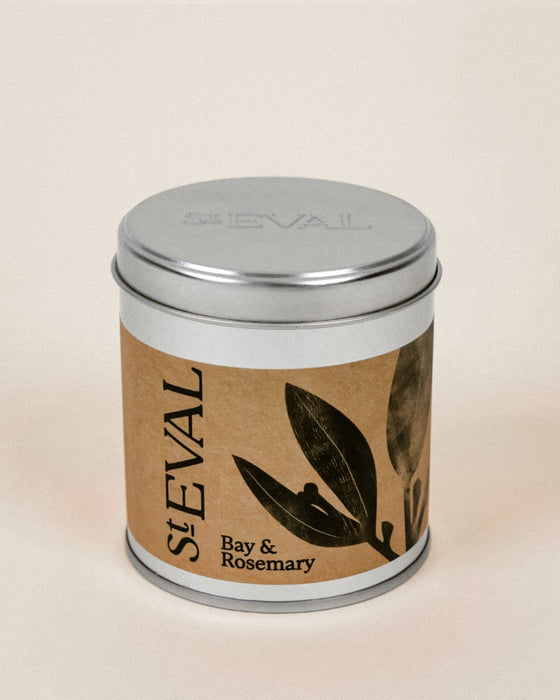 A St Eval Bay & Rosemary scented candle in a round silver metal tin with a brown kraft paper label featuring black botanical illustrations.