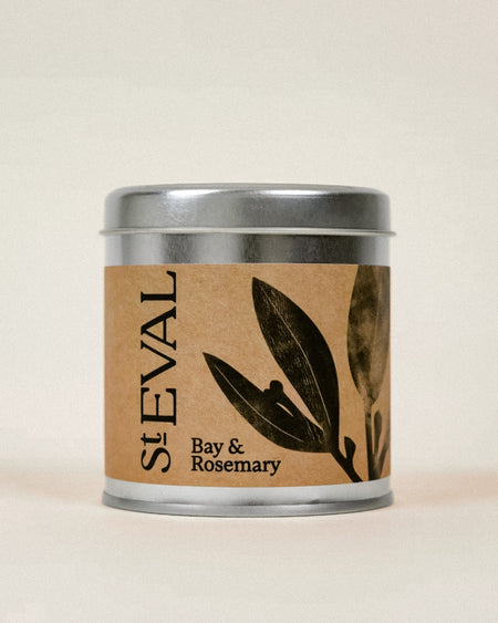 A St Eval Bay & Rosemary scented candle in a silver metal tin with a brown kraft paper label featuring black botanical illustrations.