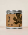 A cylindrical metal tin candle with a silver lid and base, featuring a brown kraft paper label with a dark brown fig tree leaf graphic and the text 'St EVAL Fig Tree'.