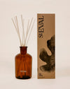 Amber glass reed diffuser bottle with white reeds next to its brown kraft paper packaging box, both featuring the brand name 'stEVAL'. Fig Tree reed diffuser by St Eval - fresh green home fragrance - Fodder