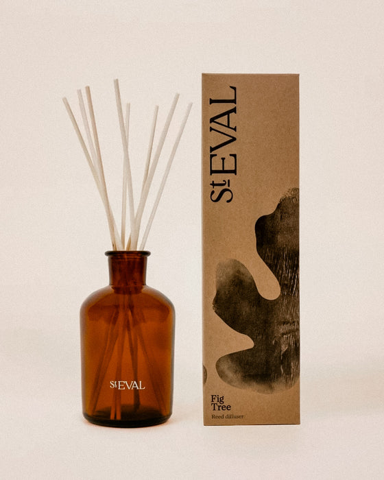 Amber glass reed diffuser bottle with white reeds next to its brown kraft paper packaging box, both featuring the brand name 'stEVAL'. Fig Tree reed diffuser by St Eval - fresh green home fragrance - Fodder