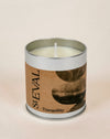A single-wick candle in a cylindrical silver metal tin with a kraft paper label reading 'StEVAL Tranquillity' and a dark abstract moon graphic, set against a warm beige background.