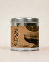 A silver metal tin candle with a brown kraft paper label that reads 'st EVAL Tranquillity' in black text, set against a plain beige background. Tranquillity scented tin candle by St Eval - illustrated tin - Fodder