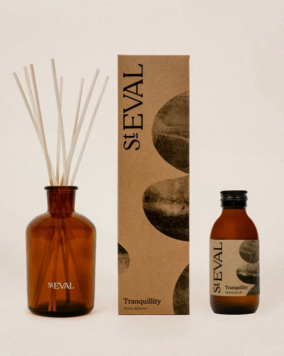 SEVAL Tranquillity reed diffuser set featuring an amber glass bottle with natural reeds, its brown kraft paper packaging box, and a smaller amber glass bottle of essential oil, all arranged on a light beige background.