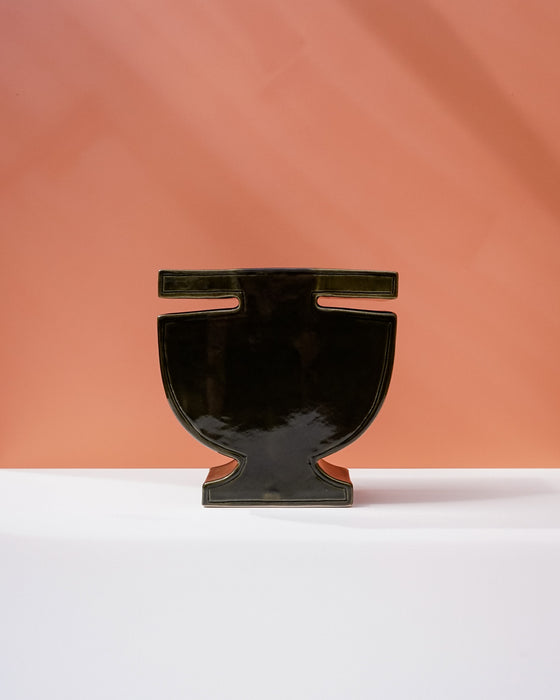 A glossy black ceramic vase with a wide, rounded body and a small rectangular handle, displayed on a white surface against a warm peach-colored background. Studio ERS | Soup Vase | Fodder