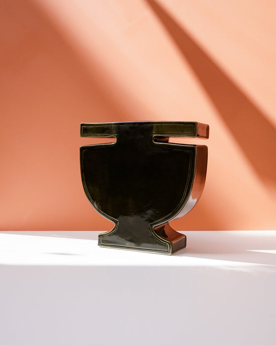 A glossy black ceramic urn-shaped vase with a wide top rim, displayed on a white surface against a terracotta-colored background with sharp diagonal shadows. Studio ERS | Soup Vase | Fodder