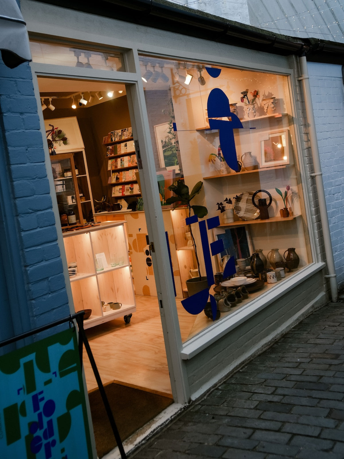 Storefront with a display of decorative items and a blue logo on the window. Fodder, homewares shop, in Hampstead, London.