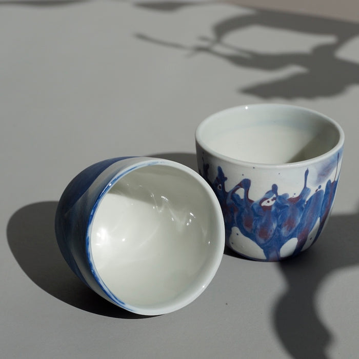 an espresso cup on a table. one of the two is on its side so you can see inside the cup. 