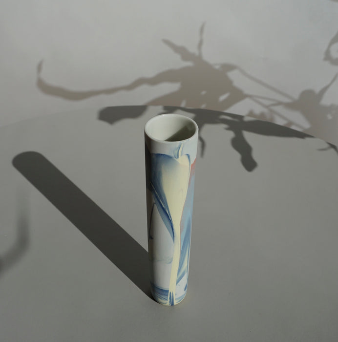 a pale pastel marble effect bud vase handmade by JDP Ceramics in Porcelain sitting on a table and casting a long shadow. 