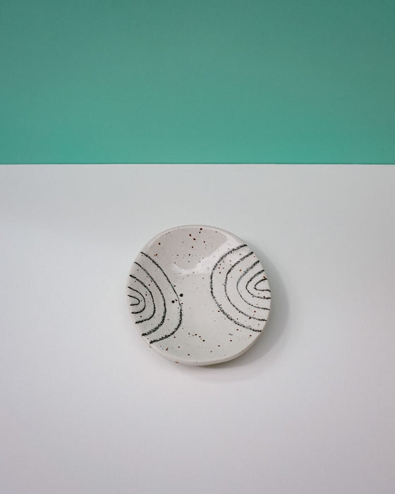 Round ceramic coaster with black patterns on a white surface with a teal background. Diddy Bowl | Jode Pankhurst | Shop Fodder