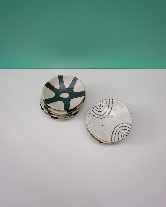 Set of ceramic coasters with abstract designs on a white surface and teal background. Diddy Bowl | Jode Pankhurst | Shop Fodder