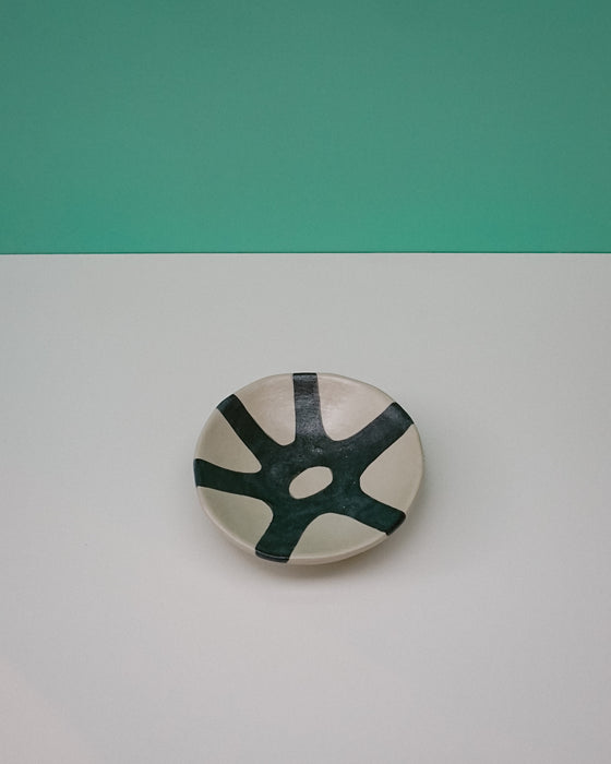 Ceramic plate with green abstract design on a white surface with teal background. Diddy Bowl | Jode Pankhurst | Shop Fodder