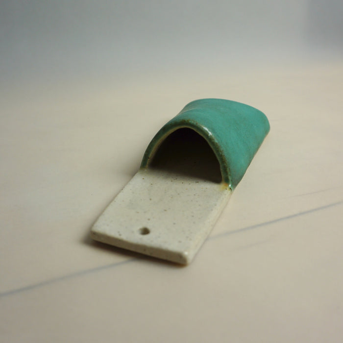 Ceramic object with green top and beige bottom on a light gray background. Pocket Wall | Jode Pankhurst | Shop Fodder
