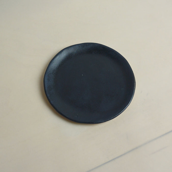 Black plate on a beige surface. Trinket Dish | Jode Pankhurst | Shop Fodder