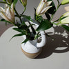 a bellied vase with an oversized round handle at the top. with a bunch of lillies. 