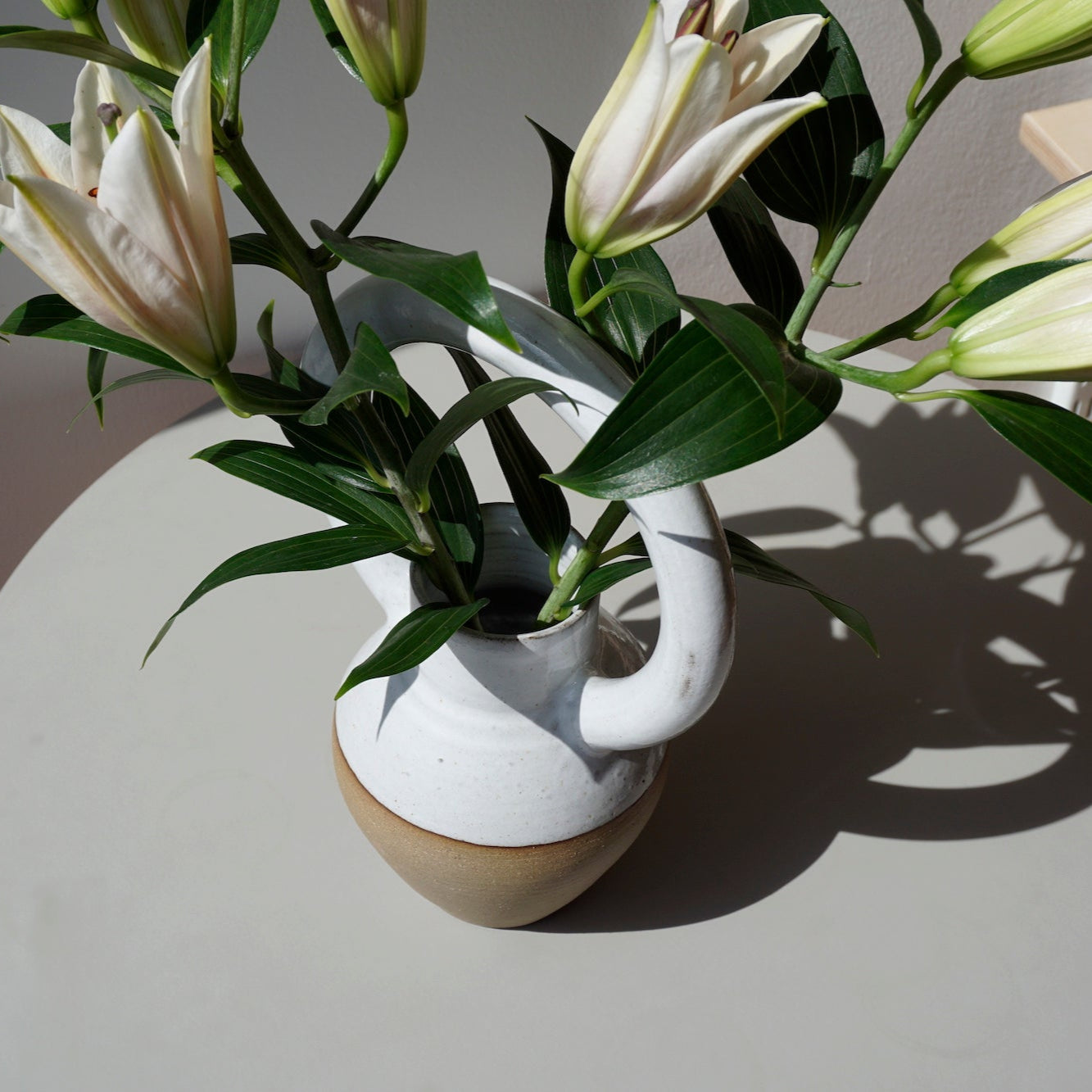 a bellied vase with an oversized round handle at the top. with a bunch of lillies. 